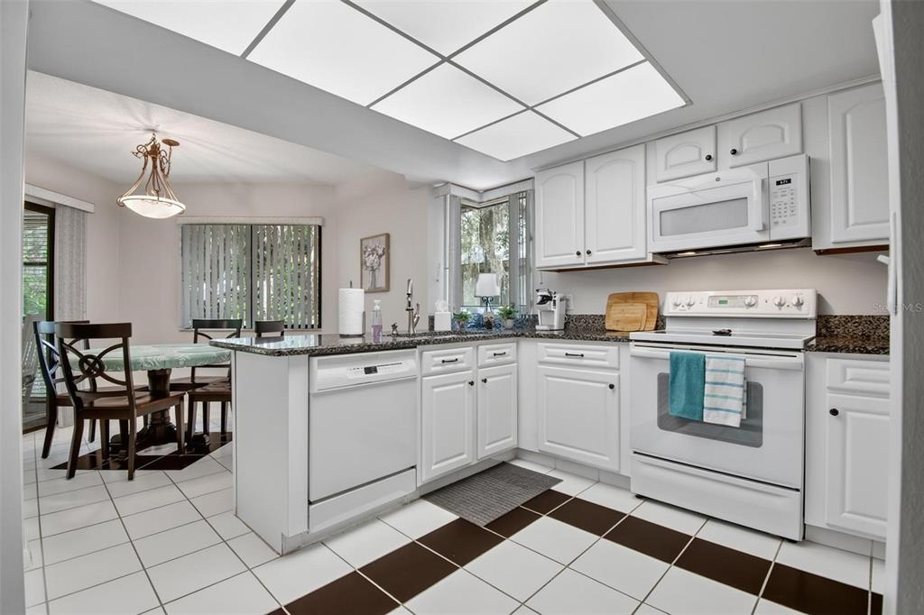 A kitchen with white cabinets, granite countertops, and a white tile floor with brown accents — 8 MID OAKS CIRCLE UNIT 8, PALM COAST, FL