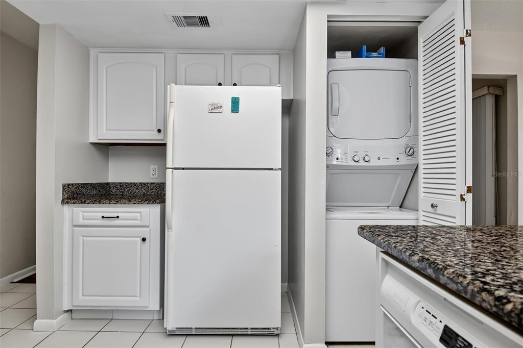A kitchen features white cabinets, granite countertops, a white refrigerator, and a stacked laundry unit — 8 MID OAKS CIRCLE UNIT 8, PALM COAST, FL
