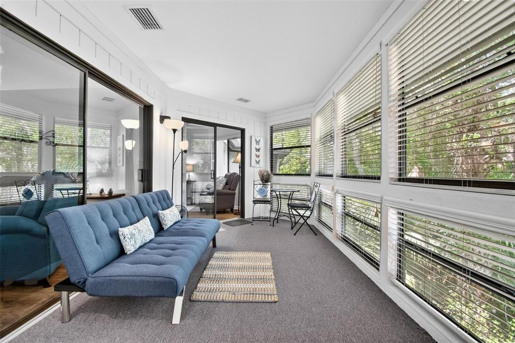 A sunroom features a blue sofa, gray carpeting, and large windows with white blinds — 8 MID OAKS CIRCLE UNIT 8, PALM COAST, FL