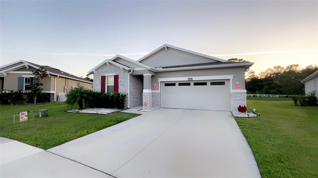 A single-story house with a white garage door, stone facade, and red shutters — 5306 MEADOW SONG DRIVE, OKAHUMPKA, FL