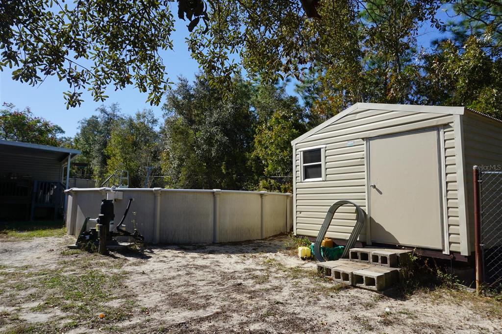 A beige storage shed stands next to an above-ground swimming pool in a sandy yard — 5012 S ORWELL POINT, HOMOSASSA, FL