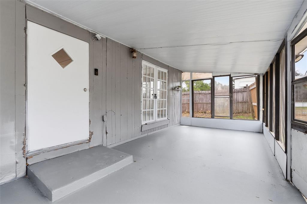 A covered porch with gray painted walls, a concrete floor, a white door, and screened windows — 37421 MARCY LANE, ZEPHYRHILLS, FL