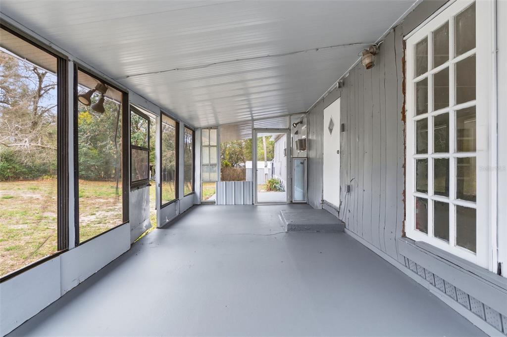 A covered screened-in porch with gray painted flooring and a white door leading inside — 37421 MARCY LANE, ZEPHYRHILLS, FL