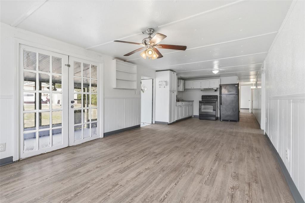 An open-concept room features white paneled walls, wood-look flooring, a ceiling fan, and a kitchen — 37421 MARCY LANE, ZEPHYRHILLS, FL
