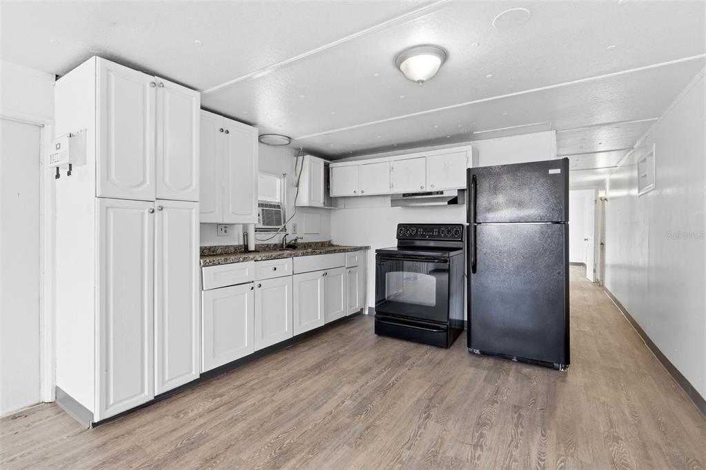 A kitchen features white cabinets, a black stove, a black refrigerator, and wood-look flooring — 37421 MARCY LANE, ZEPHYRHILLS, FL
