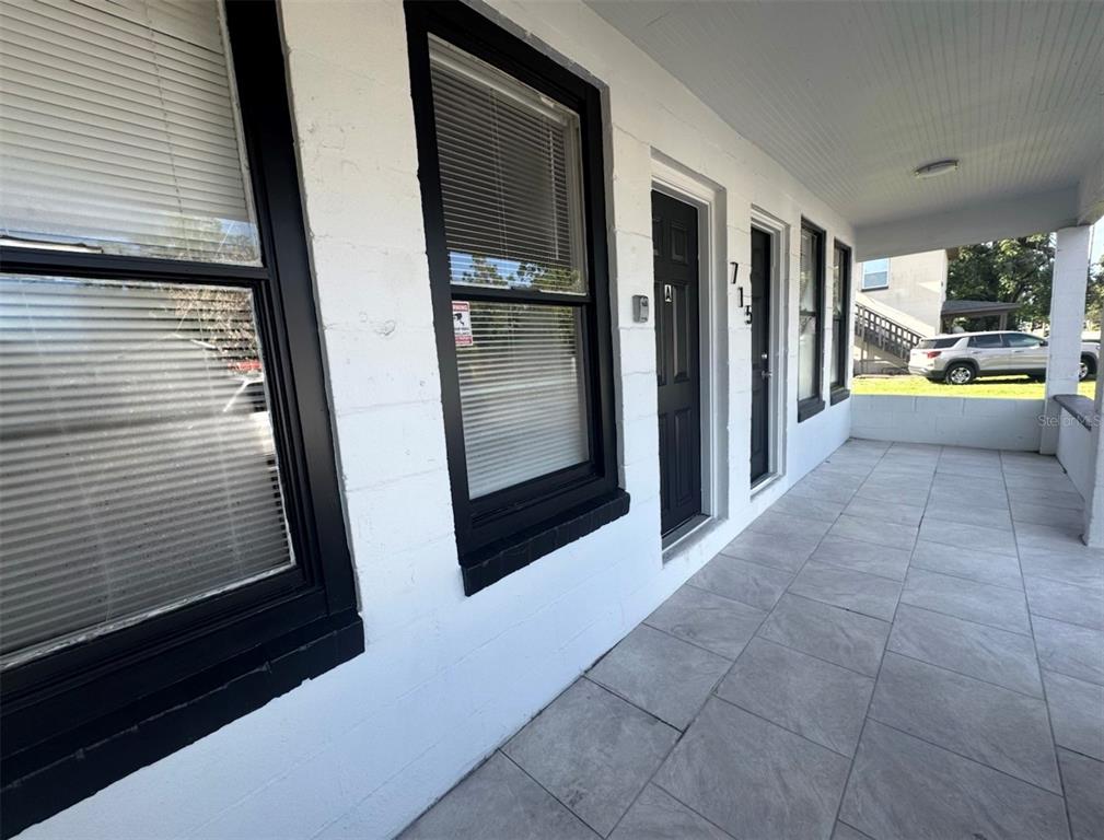 A covered porch with tiled flooring leads to two black doors on a white building — 715 JERNIGAN AVENUE, ORLANDO, FL