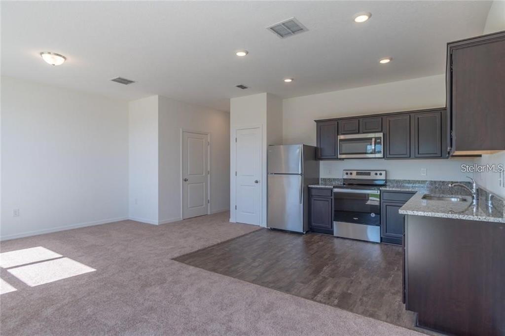 An open-concept kitchen with dark cabinets and stainless steel appliances sits beside a carpeted room — 342 MADISON DRIVE, DAVENPORT, FL