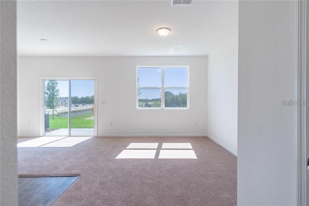 An empty living room features beige carpeting, a sliding glass door, and a window — 342 MADISON DRIVE, DAVENPORT, FL