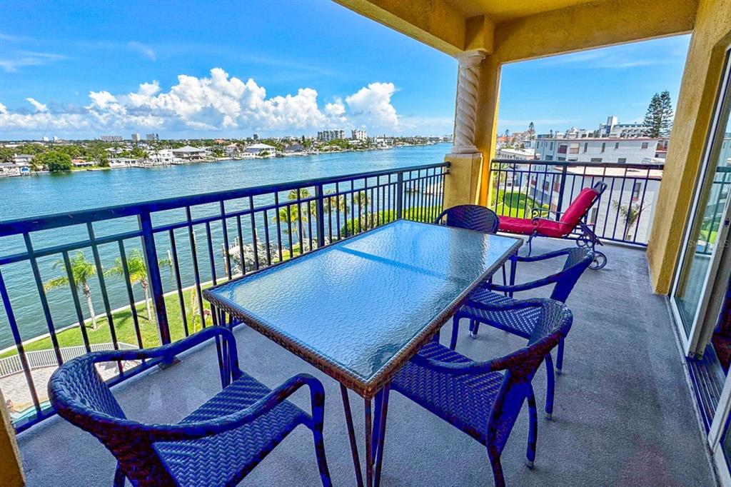 A balcony with a glass-topped dining table and chairs overlooking a waterway and buildings — 10315 GULF BOULEVARD UNIT 409, TREASURE ISLAND, FL