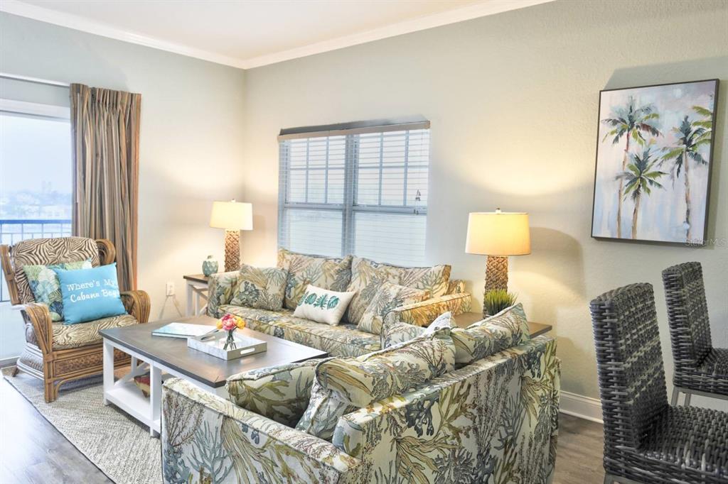 A living room with light blue walls, wood-look flooring, a ceiling fan, and balcony access — 10315 GULF BOULEVARD UNIT 409, TREASURE ISLAND, FL