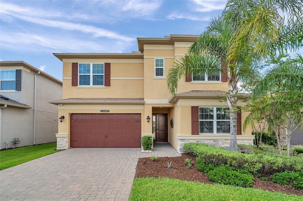 A two-story tan house with a brown garage door, stone accents, and a palm tree — 32203 MAHOGANY DRIVE, WESLEY CHAPEL, FL
