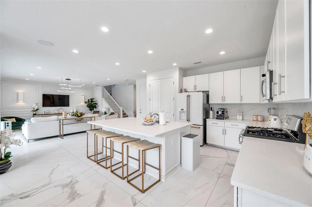 A modern open-concept kitchen features a large white island, marble-look tile floors, and white cabinetry — 32203 MAHOGANY DRIVE, WESLEY CHAPEL, FL