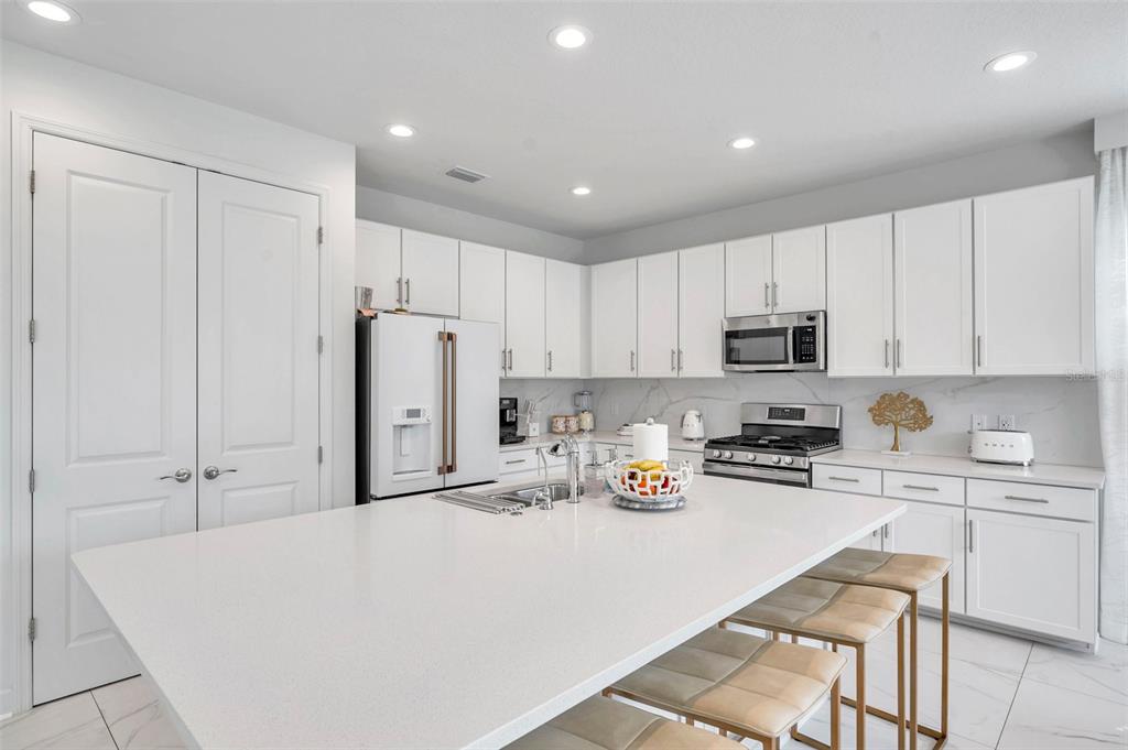 A modern kitchen features white cabinetry, a large quartz island, and stainless steel appliances — 32203 MAHOGANY DRIVE, WESLEY CHAPEL, FL