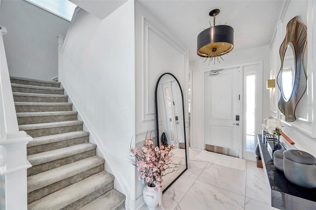 A bright entryway features a carpeted staircase, marble-look tile flooring, a modern chandelier, and mirrors — 32203 MAHOGANY DRIVE, WESLEY CHAPEL, FL