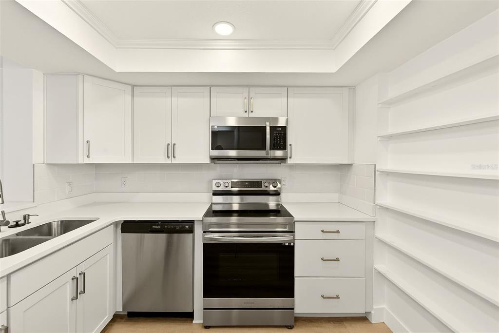 A kitchen features white cabinets, stainless steel appliances, a double sink, and open wall shelving — 16308 GULF BOULEVARD UNIT 103, REDINGTON BEACH, FL