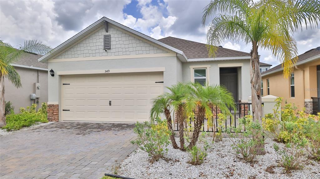 A single-story house with a beige garage, stone accents, and a palm tree in front — 349 CARYOTA COURT, NEW SMYRNA BEACH, FL