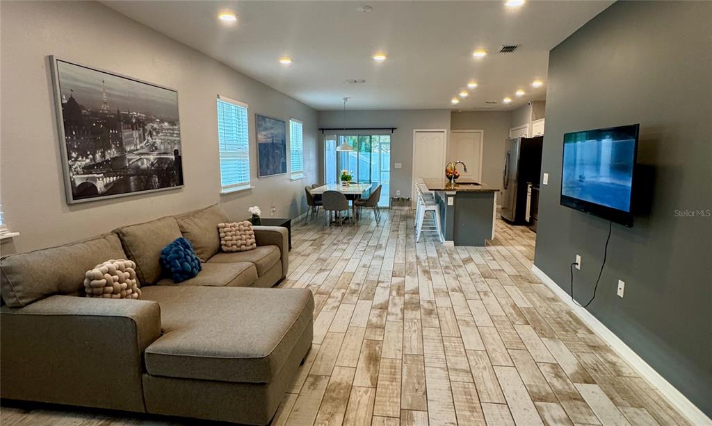 An open-concept living room and kitchen area features wood-look tile flooring and a gray accent wall — 118 HURST CT, DELAND, FL