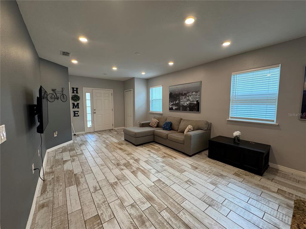 A living room features light wood-look tile flooring, a gray sectional sofa, and recessed lighting — 118 HURST CT, DELAND, FL