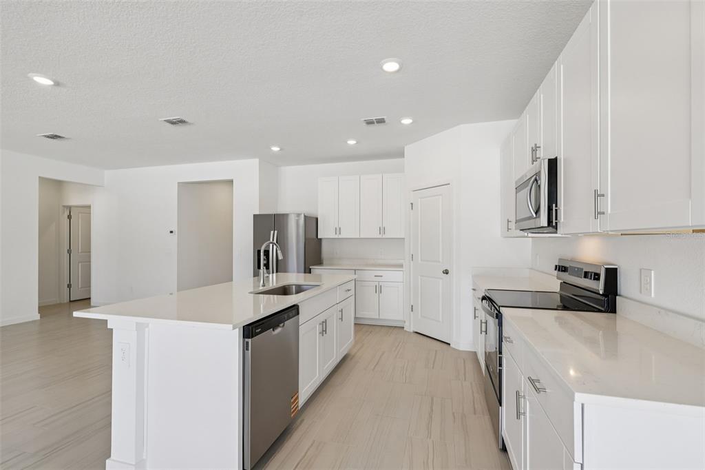 A modern kitchen features white cabinetry, stainless steel appliances, a center island, and tile flooring — 84 WANDERING CREEK WAY, PALM COAST, FL