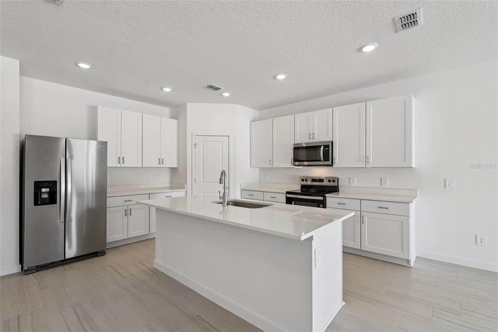 A modern kitchen features white cabinets, stainless steel appliances, a center island, and light flooring — 84 WANDERING CREEK WAY, PALM COAST, FL