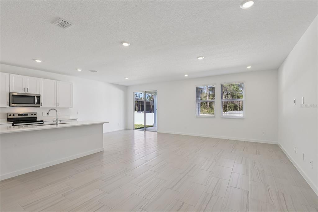 A bright, open-concept kitchen and living area with white cabinetry and light-colored tile flooring — 84 WANDERING CREEK WAY, PALM COAST, FL
