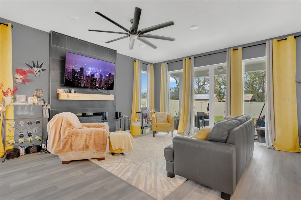 A living room features gray walls, a tiled fireplace with a television, and yellow curtains — 6213 DOLOSTONE DRIVE, LAKELAND, FL