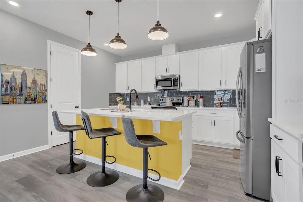 A kitchen features a yellow island with three bar stools, white cabinets, and gray flooring — 6213 DOLOSTONE DRIVE, LAKELAND, FL