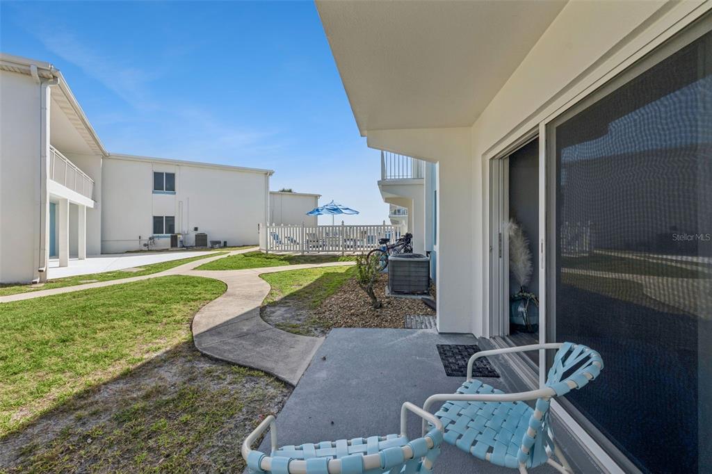 A ground-level patio with two blue chairs overlooks a grassy courtyard and a swimming pool — 513 N ATLANTIC AVENUE UNIT 33, NEW SMYRNA BEACH, FL