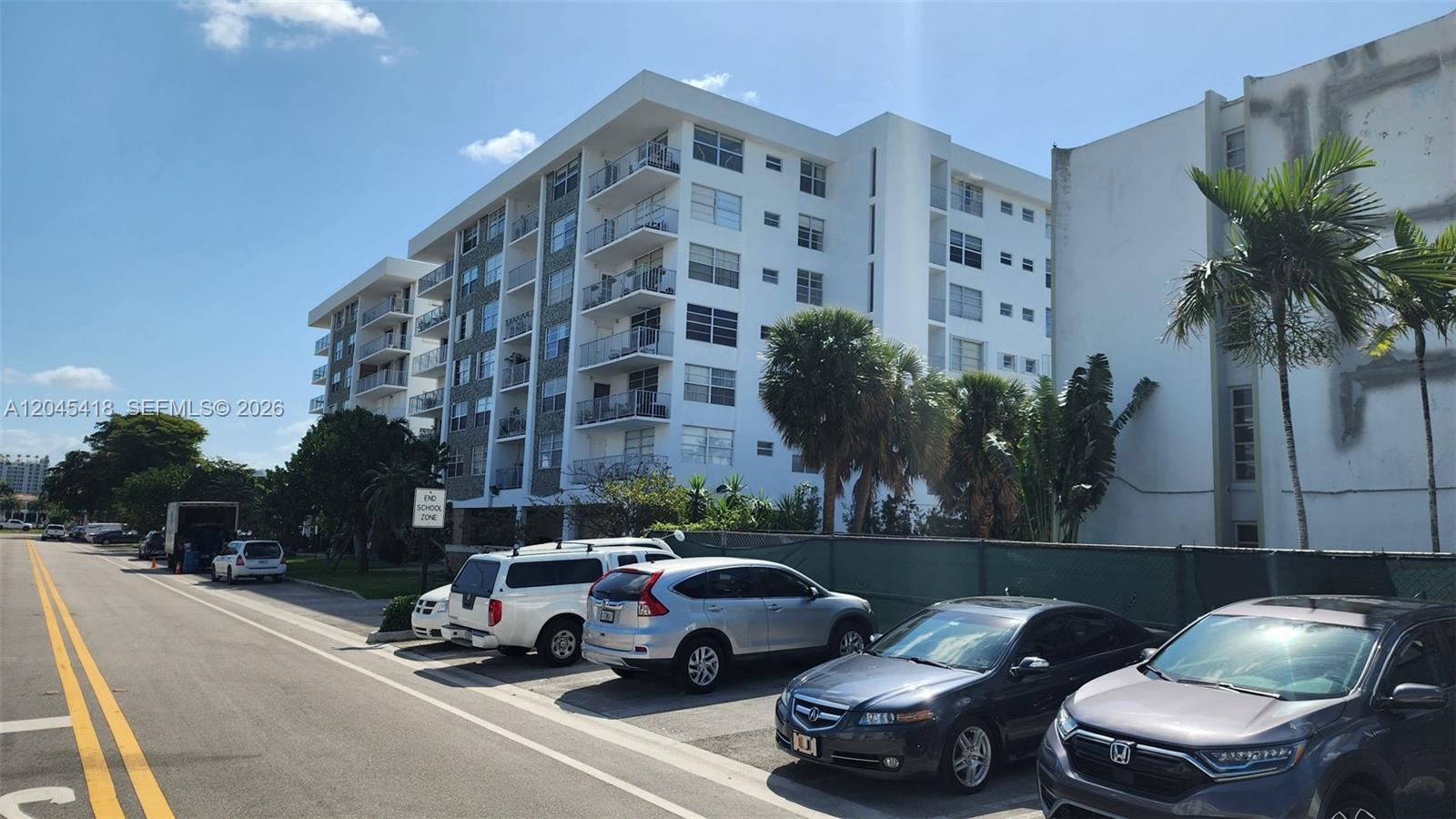A multi-story white apartment building stands behind a parking lot with several parked cars — 1075 93rd St # 304, Bay Harbor Islands FL 33154, BAY HARBOR ISLANDS, FL