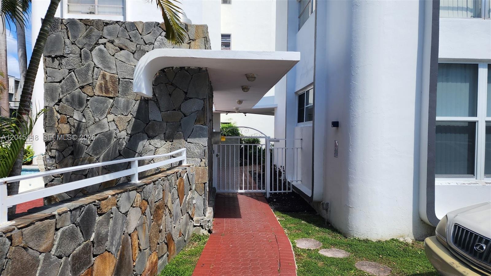 A stone wall and white building exterior lead to a gated walkway under a canopy — 1075 93rd St # 304, Bay Harbor Islands FL 33154, BAY HARBOR ISLANDS, FL
