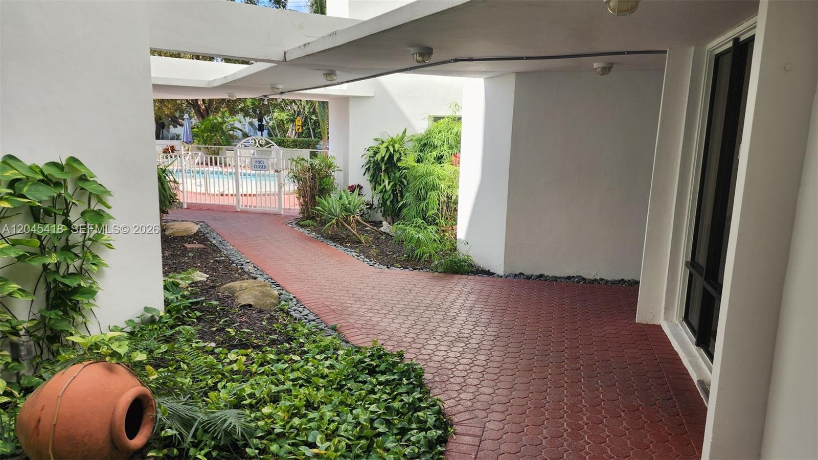 A paved walkway leads toward a gated swimming pool area under a covered building overhang — 1075 93rd St # 304, Bay Harbor Islands FL 33154, BAY HARBOR ISLANDS, FL