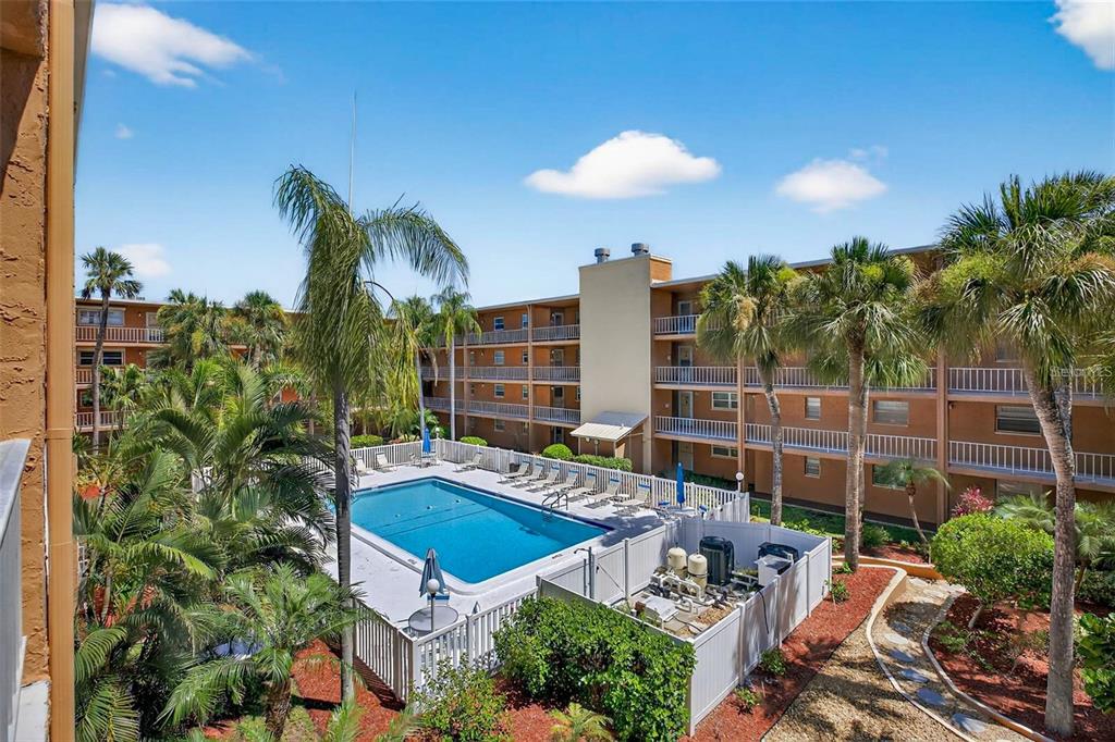 An outdoor swimming pool surrounded by palm trees and a multi-story apartment building — 12760 INDIAN ROCKS ROAD UNIT 1031, LARGO, FL