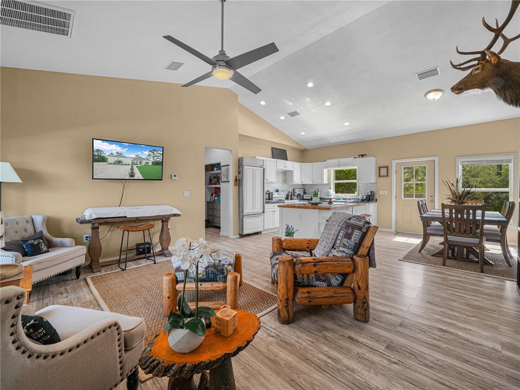 An open-concept living room and kitchen with vaulted ceilings, wood-look flooring, and rustic log furniture — 10134 S ORANGE BLOSSOM BOULEVARD, SEBRING, FL