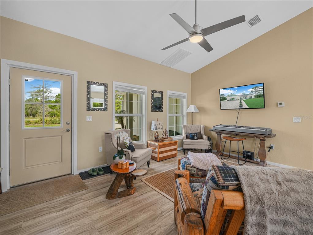 A living room features light wood-look flooring, a vaulted ceiling with a fan, and furniture — 10134 S ORANGE BLOSSOM BOULEVARD, SEBRING, FL