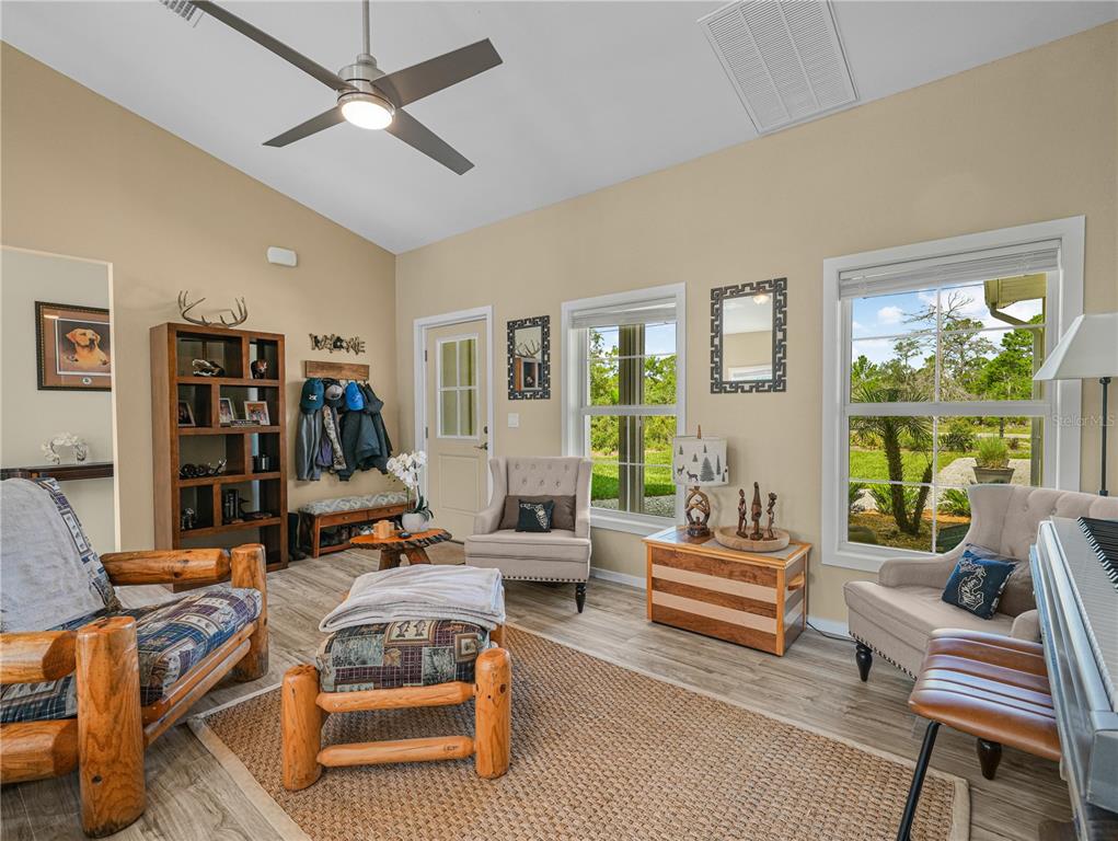 A living room features a vaulted ceiling, log-style furniture, a rug, and large windows — 10134 S ORANGE BLOSSOM BOULEVARD, SEBRING, FL