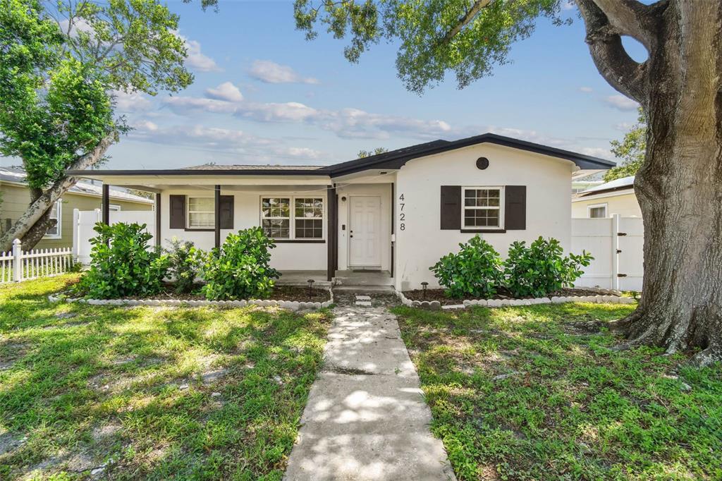 A single-story white house with a covered porch, dark shutters, and a large front tree — 4728 9TH AVENUE N, ST PETERSBURG, FL