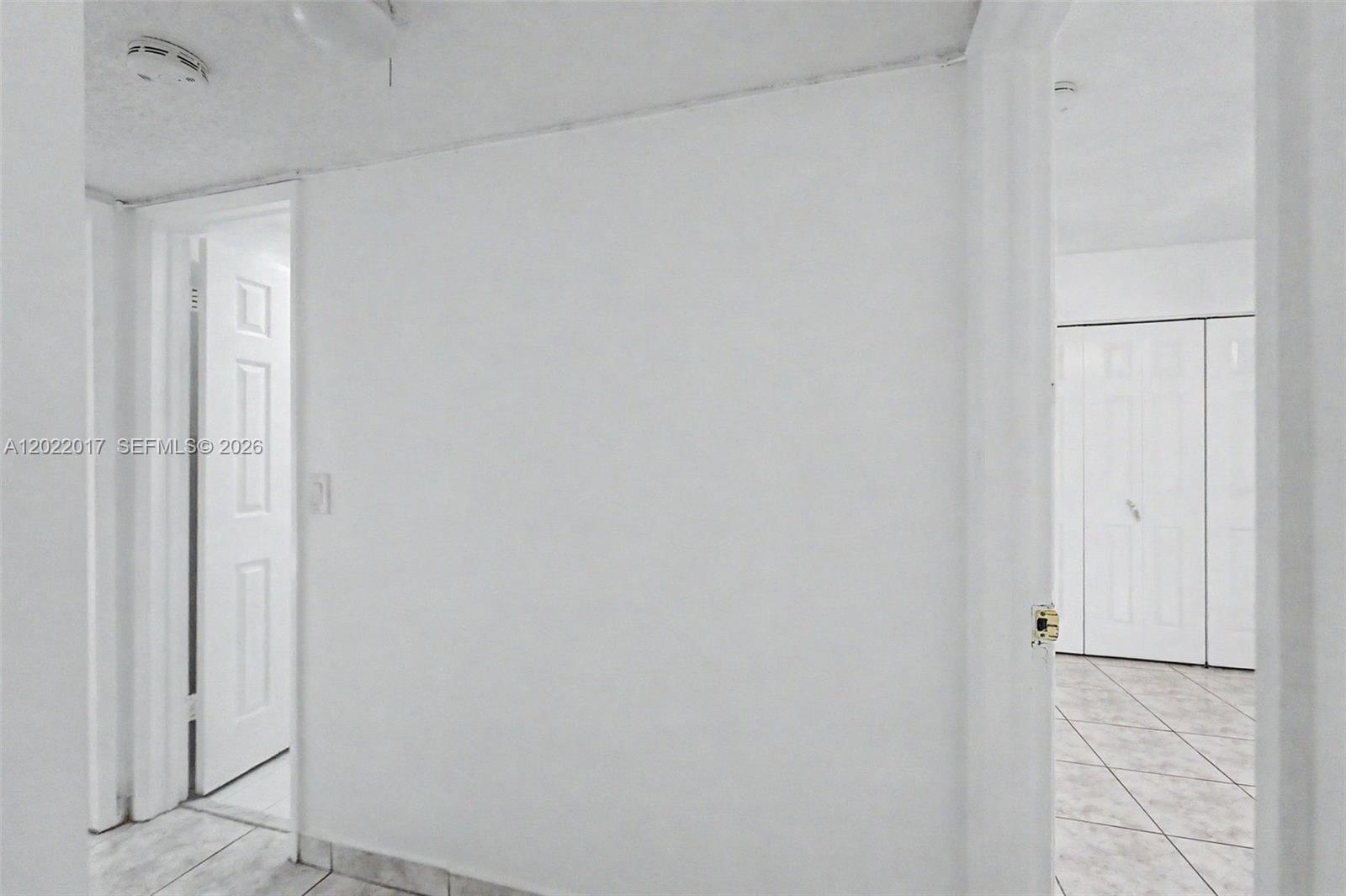 A white hallway connects to a room with tiled floors and white closet doors — 1950 W 54th St # 105, Hialeah FL 33012, HIALEAH, FL