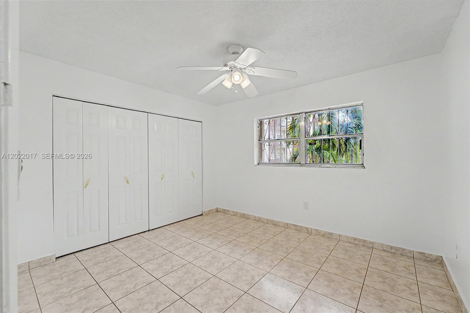 A bedroom with white walls, tile flooring, a ceiling fan, and a large closet — 1950 W 54th St # 105, Hialeah FL 33012, HIALEAH, FL