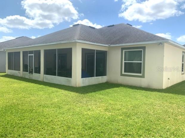 The back exterior of a beige house features a screened-in porch and a grassy yard — 406 WINDBOURNE WAY, HAINES CITY, FL