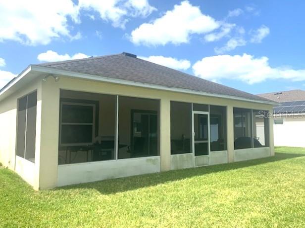 A rear view of a house with a screened-in porch and a grassy backyard — 406 WINDBOURNE WAY, HAINES CITY, FL