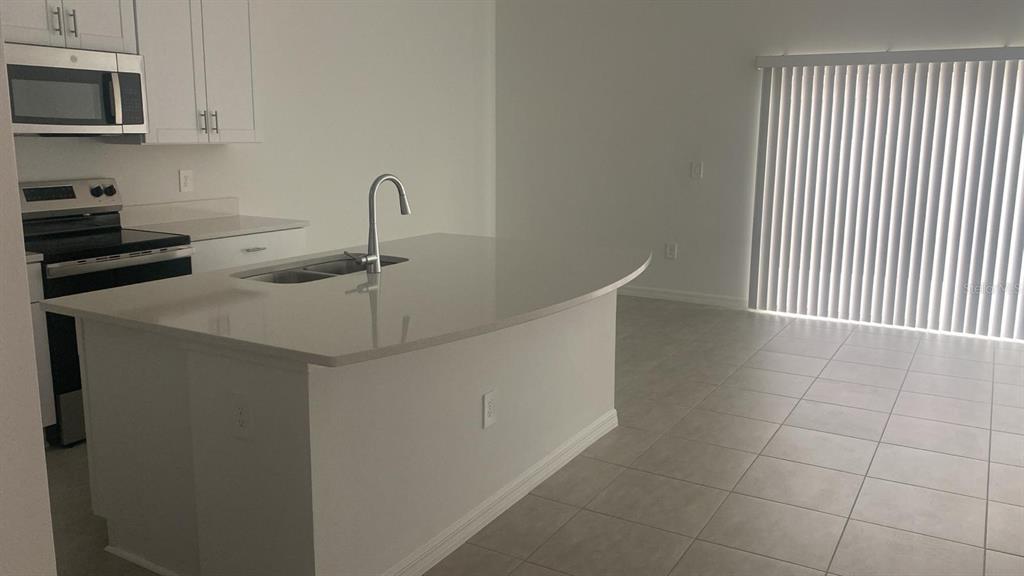 A kitchen features a curved island with a sink, white cabinetry, and tile flooring — 3606 MAYFAIR STREET, KISSIMMEE, FL
