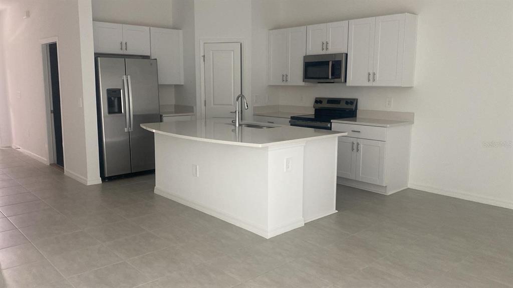 A modern kitchen features white cabinets, stainless steel appliances, and a central island with seating — 3606 MAYFAIR STREET, KISSIMMEE, FL