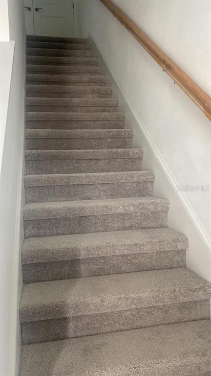 A carpeted staircase with a wooden handrail leads to a closed door at the top — 3606 MAYFAIR STREET, KISSIMMEE, FL