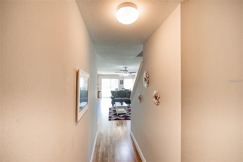 A hallway with light wood flooring leads to a living room with a ceiling fan — 4514 LIMERICK DRIVE, TAMPA, FL