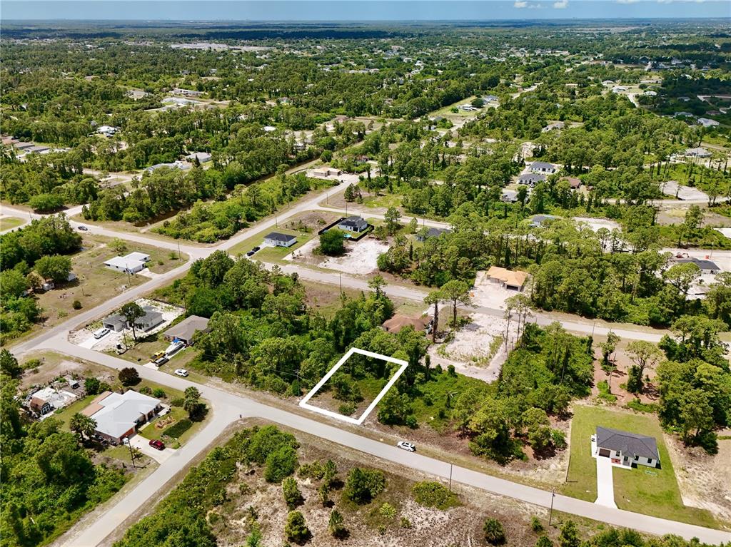 An aerial view shows a vacant, rectangular lot outlined in white within a wooded neighborhood — 460 NORWOOD AVENUE S, LEHIGH ACRES, FL