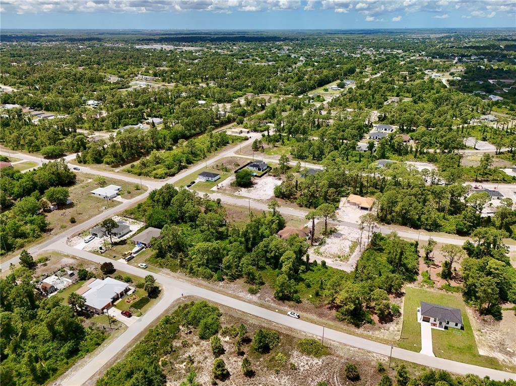 An aerial view shows a residential neighborhood with scattered houses, paved roads, and wooded lots — 460 NORWOOD AVENUE S, LEHIGH ACRES, FL