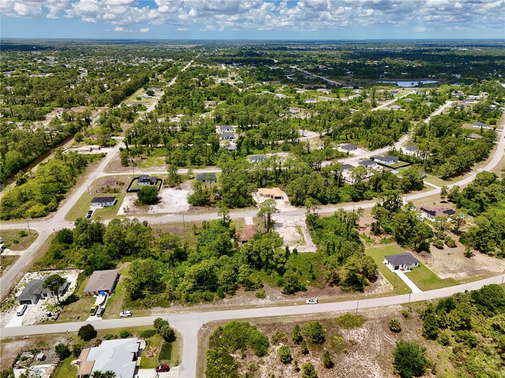An aerial view shows a residential neighborhood with scattered houses surrounded by dense green trees — 460 NORWOOD AVENUE S, LEHIGH ACRES, FL