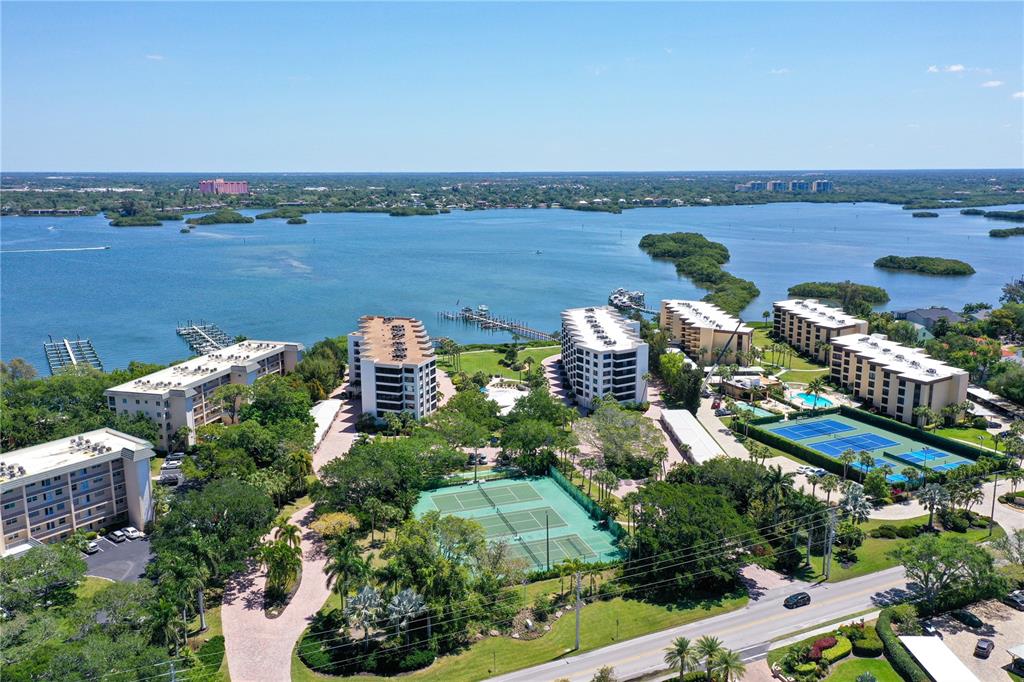 An aerial view shows several multi-story residential buildings, tennis courts, and a waterfront dock — 8735 MIDNIGHT PASS ROAD UNIT 105B, SARASOTA, FL