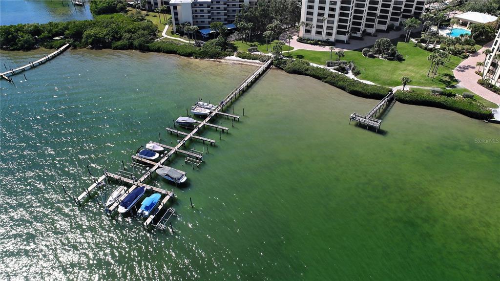 An aerial view shows a long wooden dock with several boats moored in calm water — 8735 MIDNIGHT PASS ROAD UNIT 105B, SARASOTA, FL