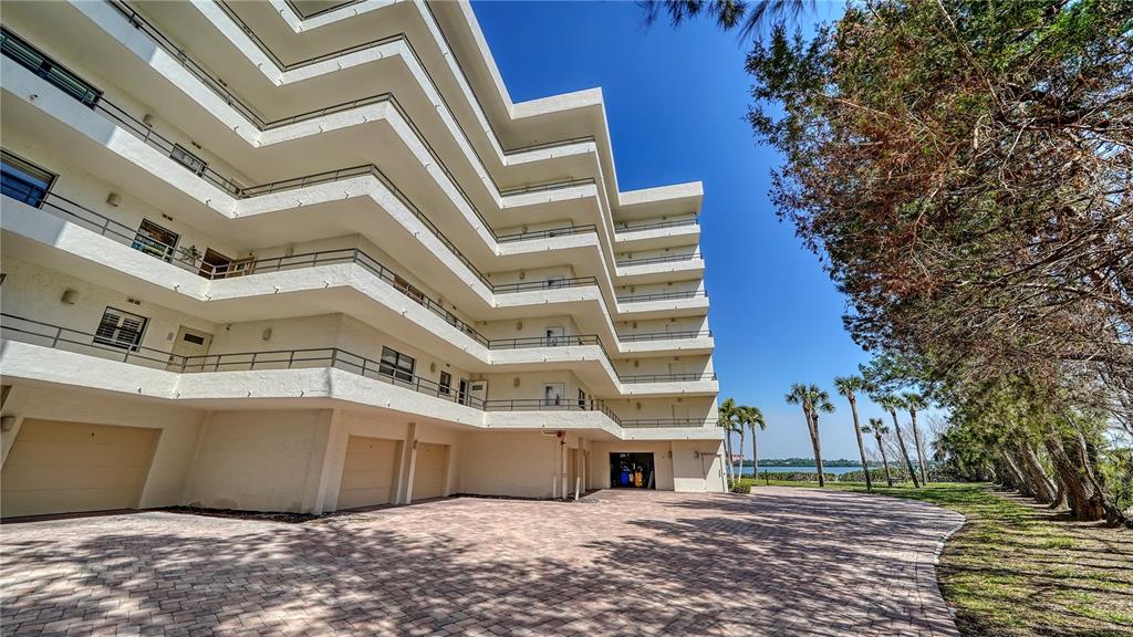 A multi-story white apartment building with tiered balconies sits next to a paved driveway — 8735 MIDNIGHT PASS ROAD UNIT 105B, SARASOTA, FL